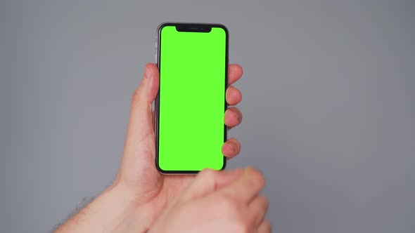 Male Hands Using a Smartphone with a Green Screen on a Gray Background. Chroma Key alt