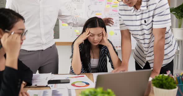 Frustrated young asian businesswoman touching her forehead while his colleague consoling her. alt