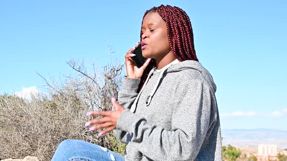 Young Black Woman Sitting One Stone and Arguing Using Phone