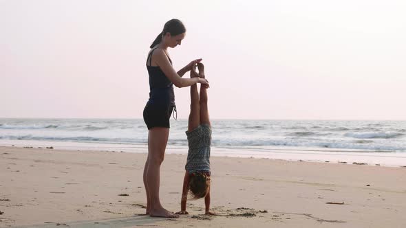 Young Sporty Mother with Little Daughter Doing Gymnastic on the Beach