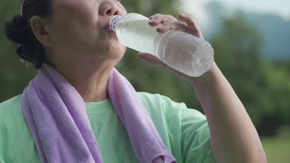 Close up Asian senior woman drink water from plastic bottle after exercise at the park alt