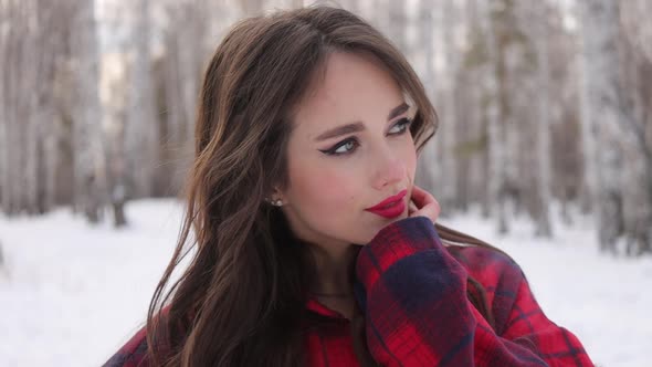 Young Woman with Wavy Hair Standing and Touching Face in Winter Forest