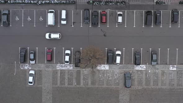 A White Car Drives Along an Asphalt Road Along Parked Cars in a Large Parking Lot alt