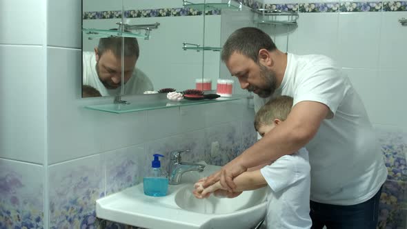 Dad washes a small child's hands with soap over the sink with running water. Personal hygiene