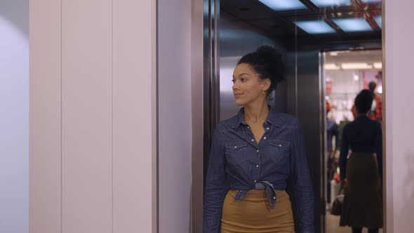 A Young African American Woman Exits an Elevator and Enters a Women's Clothing Store in a Mall alt