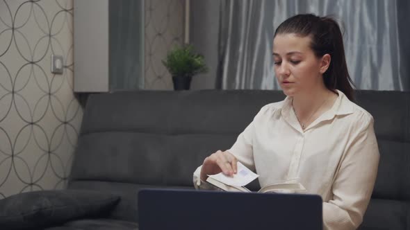 Young Woman Making Notes in Notepad at Home