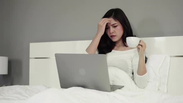 panning shot of woman drinking a cup of coffee and using a laptop computer on bed