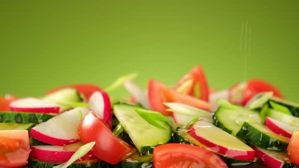 Pouring olive oil on fresh vegetables salad, green background alt