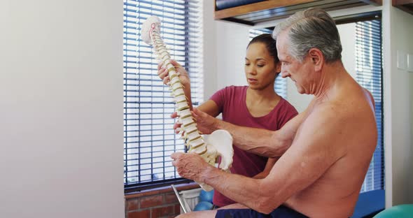 Physiotherapist explaining the spine model to senior patient 4k alt
