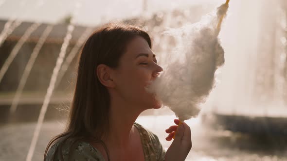 Attractive Woman Eats Cotton Candy Against Blurry Fountain alt