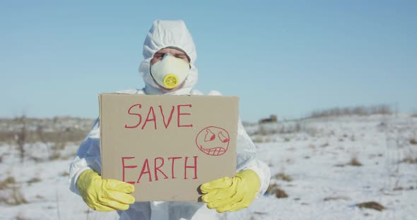 Man Wore in Protective Suit Shows Save Earth Sign on Abandoned Place in Winter alt