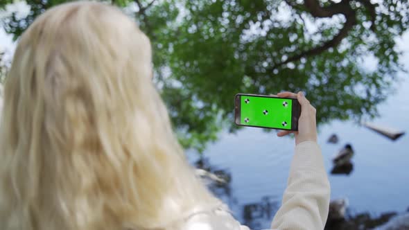 Curly Blonde Woman Holding a Phone with a Green Screen in the Street