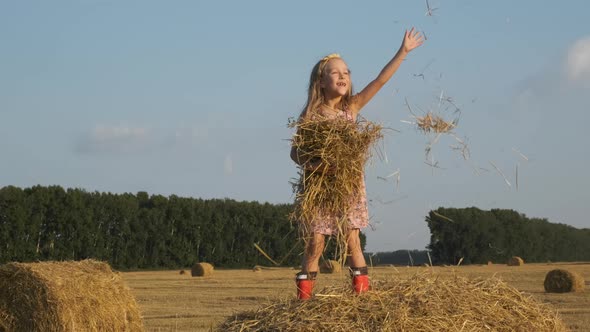 Little Girl Throwing Hay Up in a Harvested Field alt