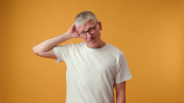 Close Up Portrait of Thoughtful Senior Man Rubbing Head Against Yellow Background