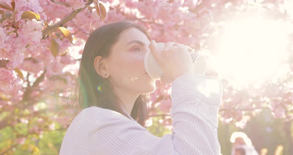 Charming lady drinking coffee and resting in a blooming garden on at sunny day alt