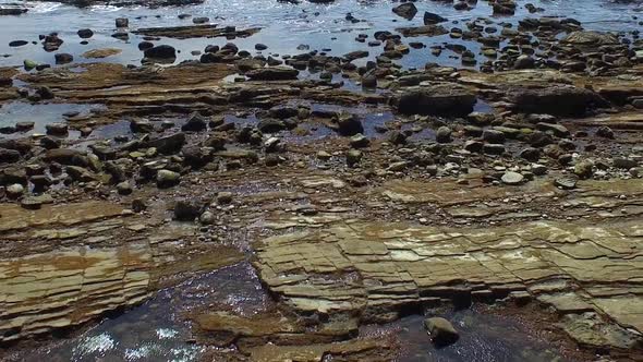 Side view tracking shot of a young man running on a rocky ocean beach shoreline. alt