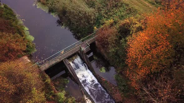 Water flowing through a little canal, passing a dam. Aerial shot 4k alt