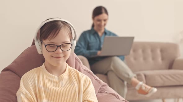 Girl with Down Syndrome Listening to Music in Headphones at Home alt
