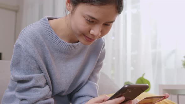 Young Asian woman holding smartphone and credit card with paying for shopping online. alt