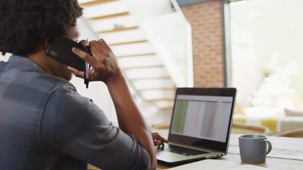 African american man working from home and using laptop and smartphone alt