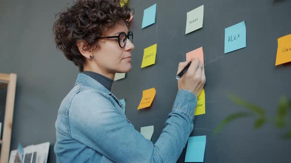 Young Woman Writing on Sticky Notes Planning Business in Modern Creative Office alt