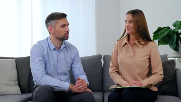 Man Patient and Woman Psychologist Sitting on Couch Talking and Turn to Camera alt