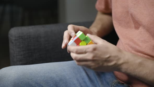 Young male hands turn and twist sides of Rubik’s cube, seen from side alt