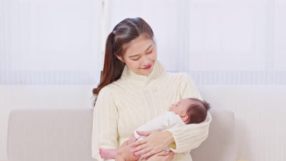 Beautiful Asian mom woman holding newborn baby in her arms sit on bed alt