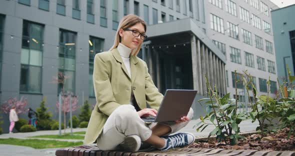 Young Caucasian Female Freelancer Typing on Keyboard Using Laptop Computer. Outdoors. alt