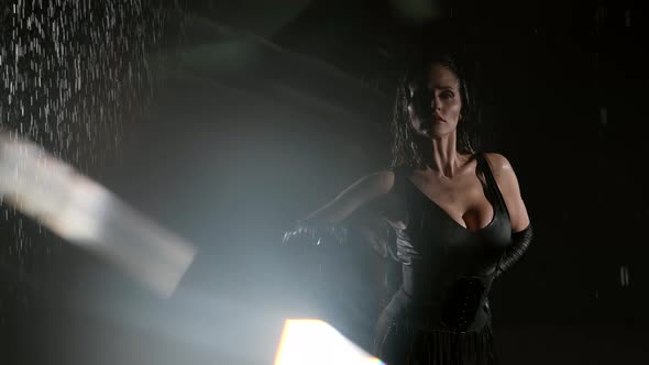 A Beautiful Busty Woman in a Black Suit Poses Against a Dark Background While Raindrops Pour Down on alt