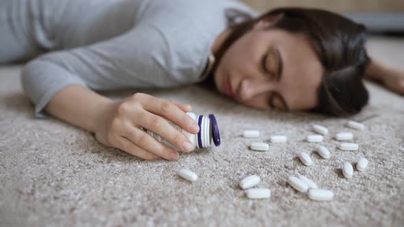 Unconscious Woman with Pills in Her Hands Lies on the Floor alt
