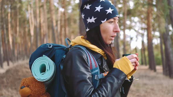 Woman Hiker Having Rest with Hot Drink Tea From Thermos on the Pine Forest alt