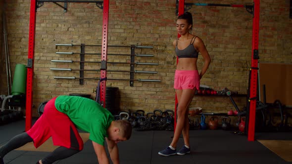 Fitness Instructor Explaining and Showing Exercise to Fit Woman in Health Club alt