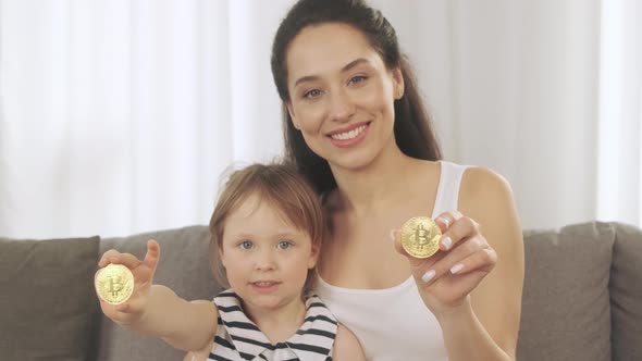A Young Mother and Her Daughter Show Bitcoin in Their Hand alt