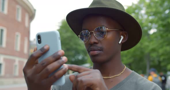 Close Up Portrait of Smiling Young African Man with Smartphone and Earphones Outdoors alt