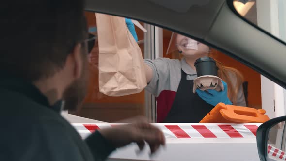 Staff with Protective Mask Serving Takeaway Order To Customer at Drive Thru Counter alt