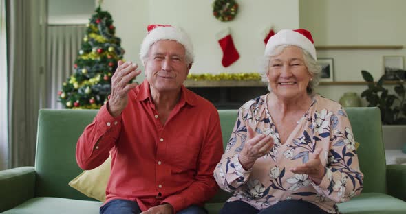 Happy caucasian senior couple in santa hats on video call at christmas time alt