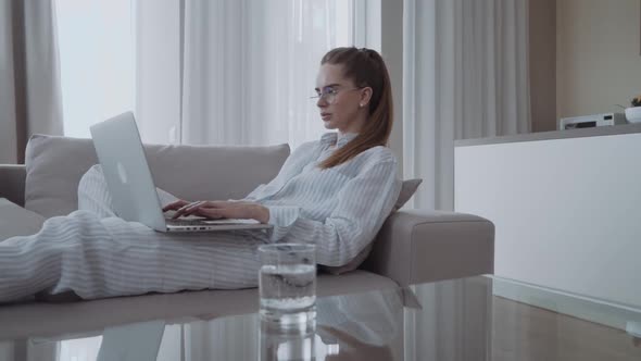 Serious Attractive Young Woman Sitting on Sofa Using Laptop Communicating Working Online at Home alt