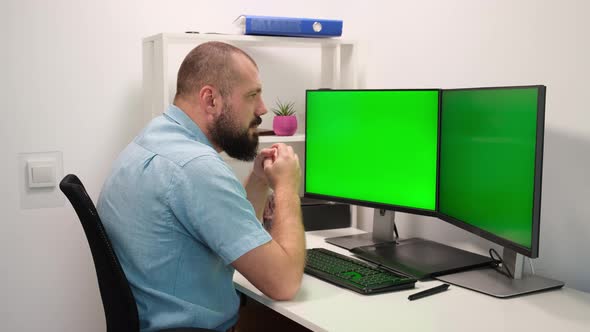 Man typing on the keyboard on two monitors with the green screen. remote work at home alt