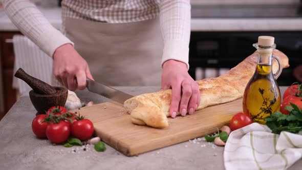Woman Slicing Baguette on Wooden Cutting Board at Domestic Kitchen alt