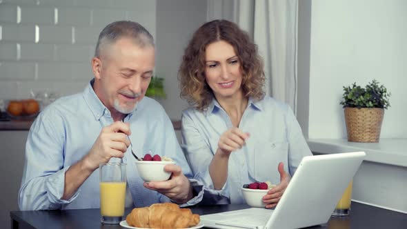 A Happy Middleaged Couple is Having Breakfast and Watching a Laptop