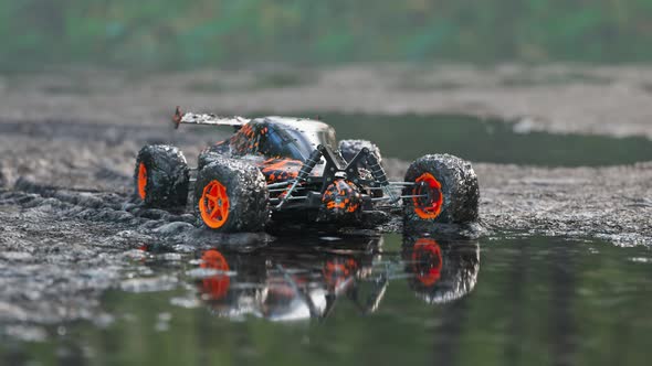 Dirty, orange RC-Car got stuck in the mud on a wet forest mire path. 4KHD alt