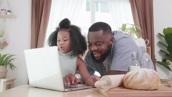 African American dad teaching girl doing homework online at the home kitchen table