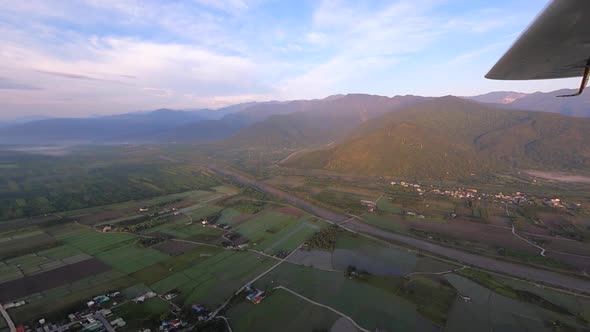 Aircraft flying over farmland in valley during sunrise hour filmed as wide angle point of view from alt