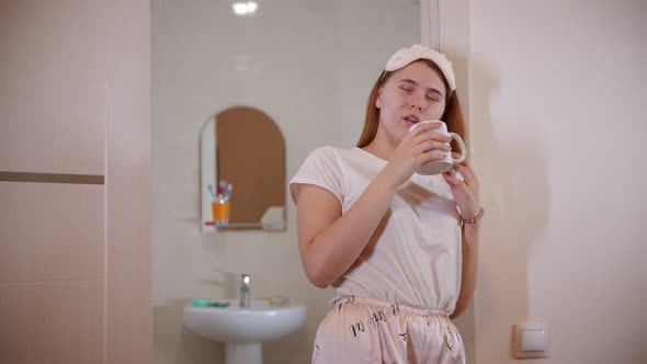 A Young Woman Drinking Coffee Standing in the Bathroom Doorway at the Morning alt