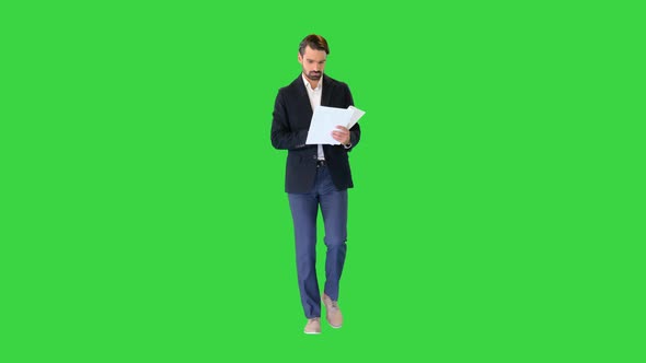 Serious Young Businessman Reading Documents While Walking on a Green Screen Chroma Key alt