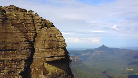 Drone circling cliff face revealing mountains and rocky escarpments in the background. Location NSW, alt