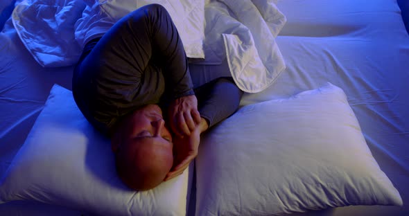 Close-up Portrait of a Bald, Middle-aged Man Lying in Bed with White Linens and Two Pillows. He's alt