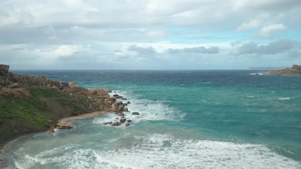 AERIAL: Mediterranean Sea Rolls Waves to Ghajn Tuffieha Bay on a Rocky Beach