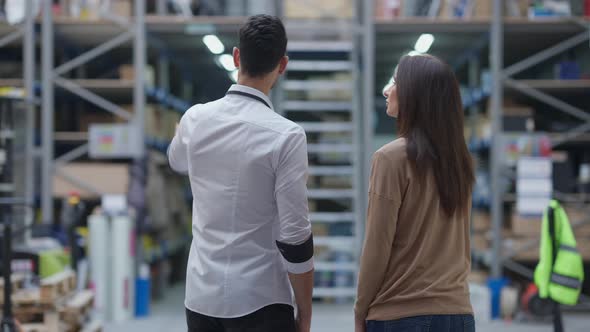 Back View of Concentrated Man and Woman Pointing at Racks in Warehouse Talking alt
